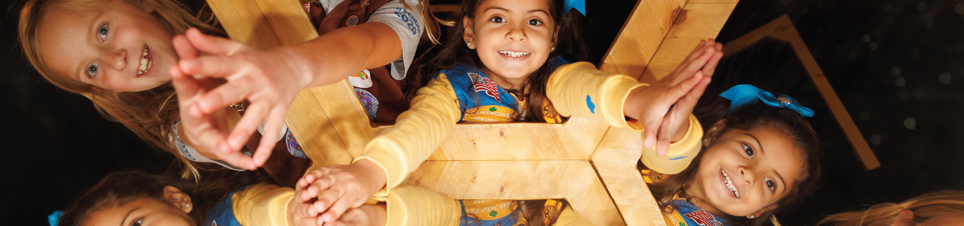  Group of kindergarten daisy girl scouts in vest and apron uniform hugging and smiling outside. 