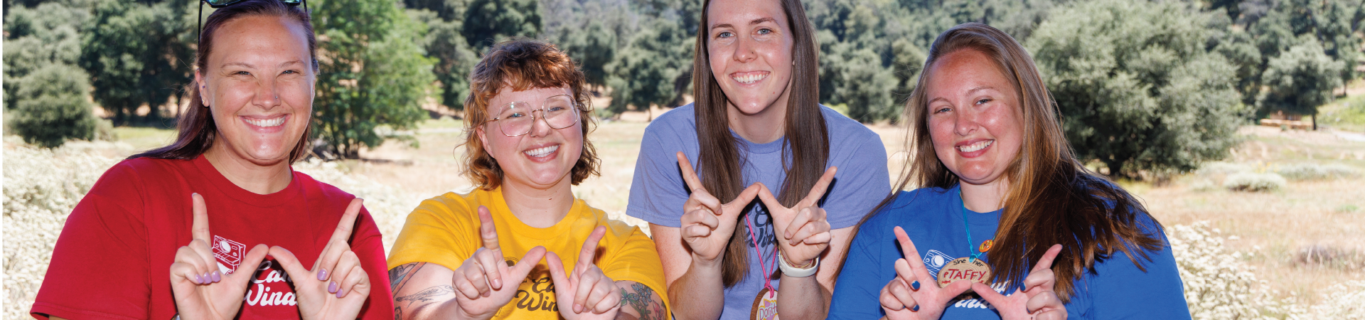  adult volunteer wearing vest with a girl scout junior (right, in baseball cap) and daisy (left) outside at a park smiling and looking at one another 