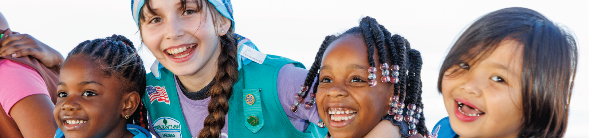  two girl scouts wearing trefoil clothing leaning on one another indoors 