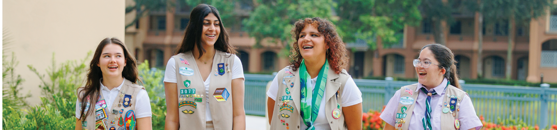  two senior girl scouts wearing sash uniforms outside standing back to back and smiling at the camera 